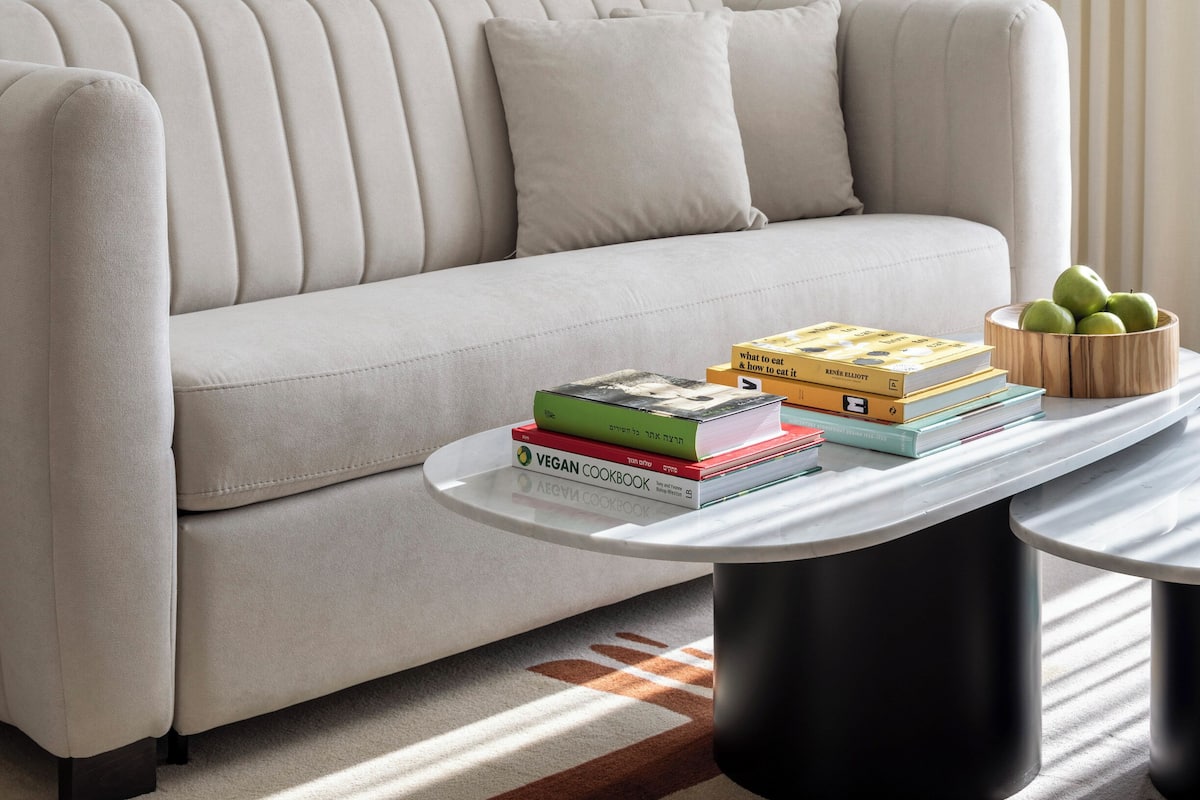 A modern living room with a sofa, a coffee table with books, and a framed abstract painting.