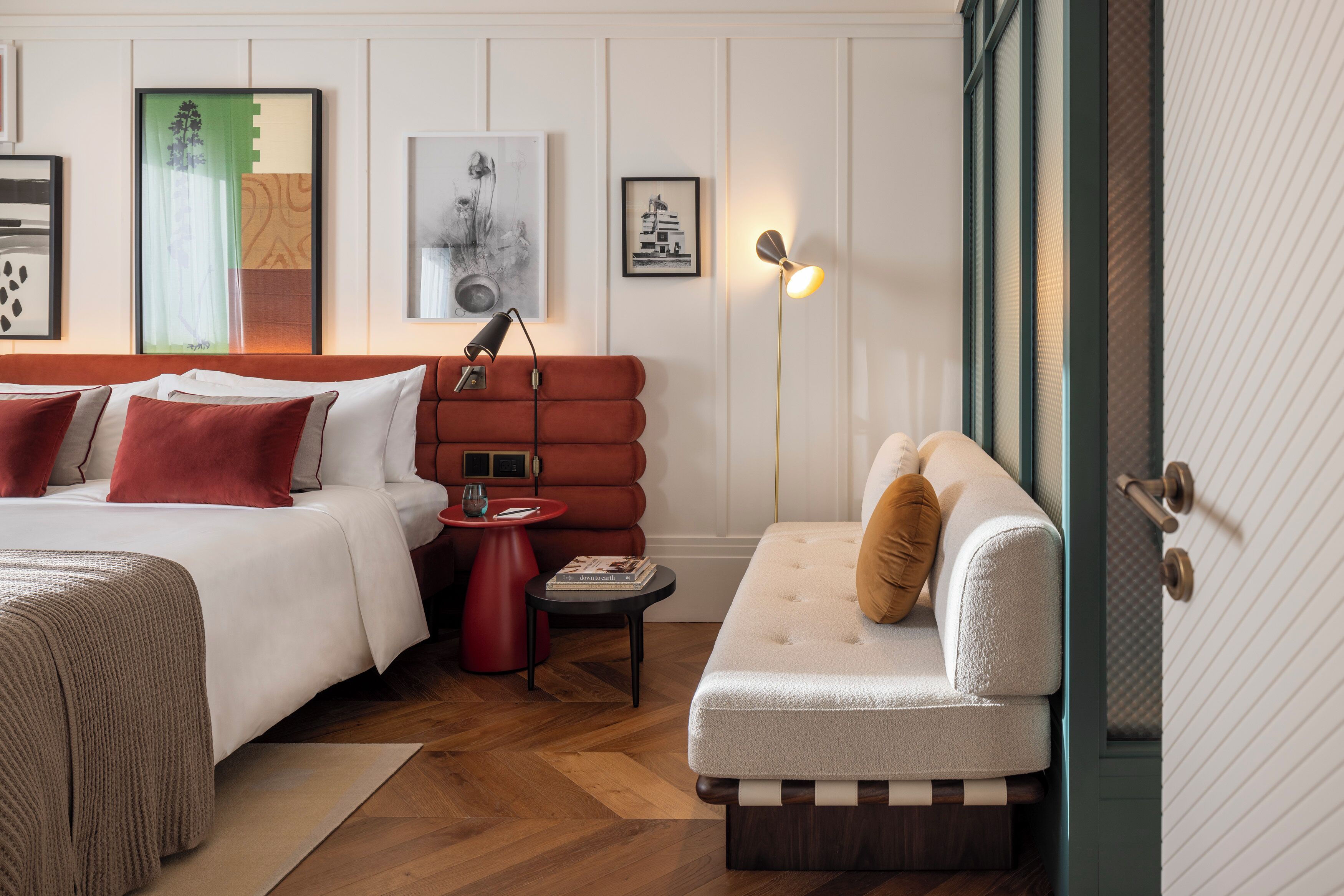 A modern hotel room with a bed, a sofa, a small table, and a lamp.