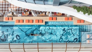 An aerial view of a swimming pool with a tiled deck, lounge chairs, and a person swimming. - The George Tel Aviv (Tel Aviv)