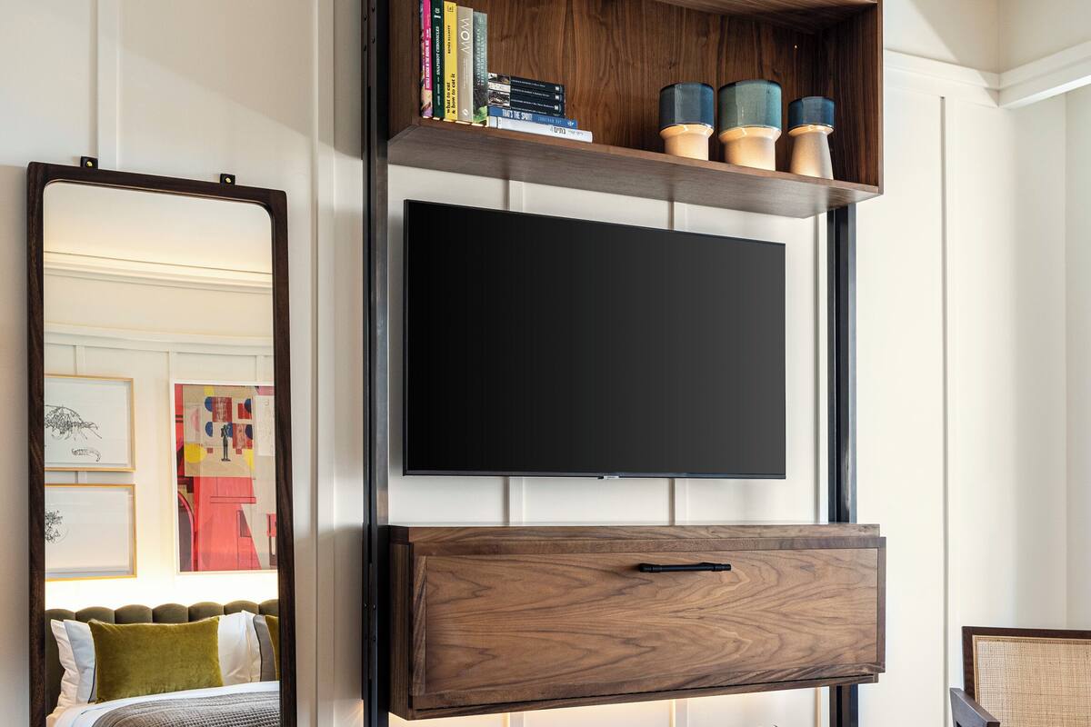 A modern bedroom with a large bed, a wooden TV stand, a mirror, and a bookshelf.