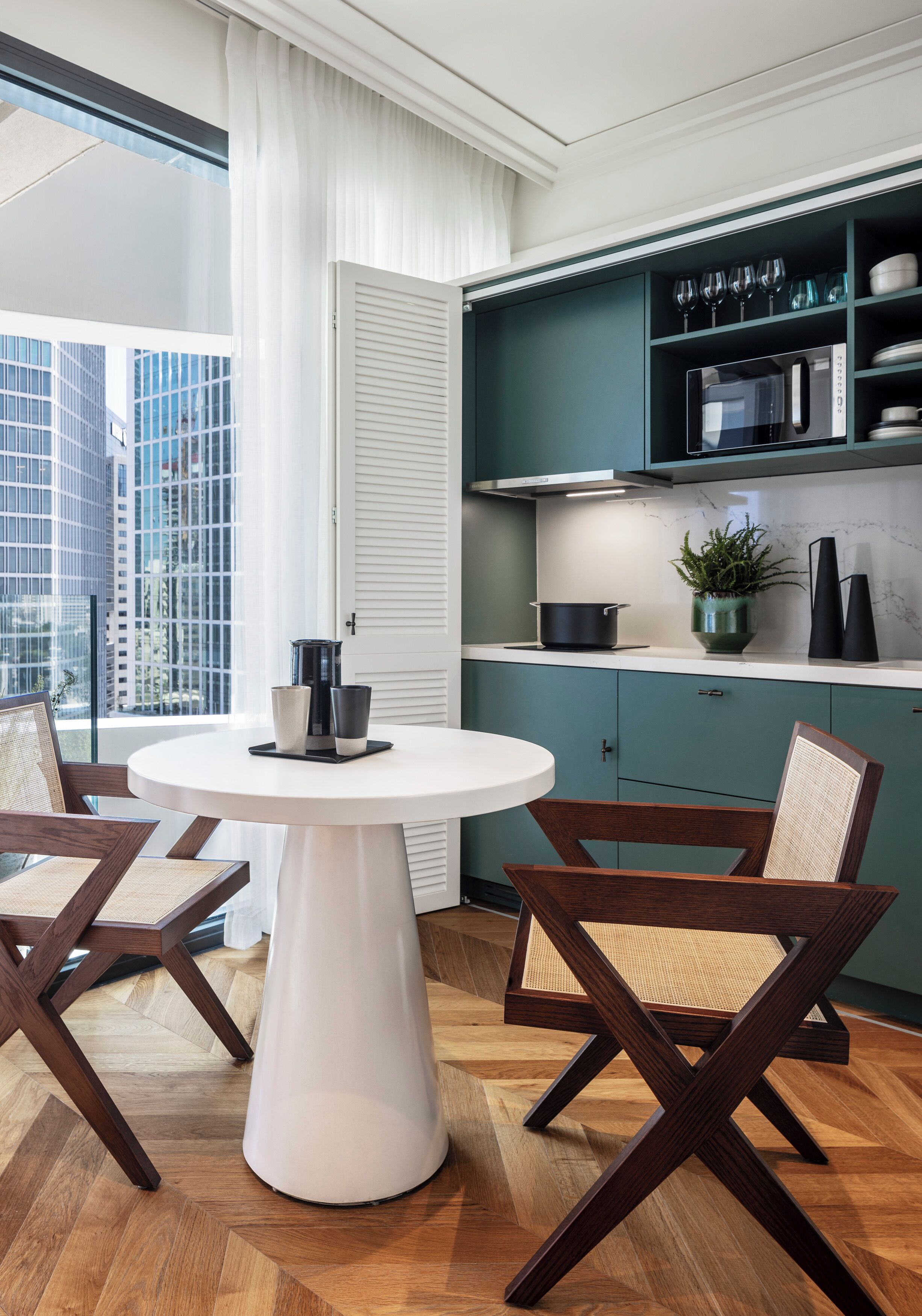 A modern kitchen with teal cabinets, a white countertop, and a round dining table with two chairs.