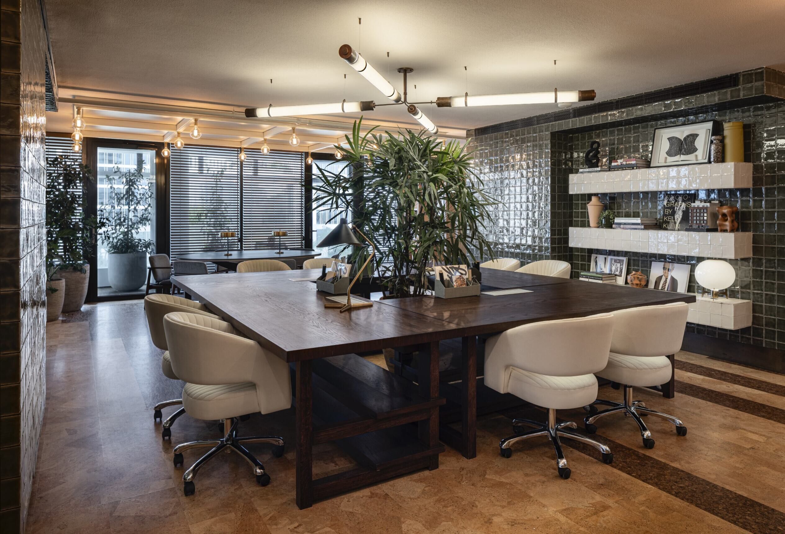 A modern conference room with a dark wooden table, white leather chairs, and a large potted plant.