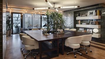 A modern conference room with a dark wooden table, white leather chairs, and a large potted plant.