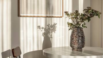 Een eetgedeelte met een ronde tafel, twee stoelen, een vaas met bloemen en een ingelijst schilderij aan de muur.