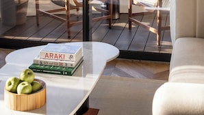 A modern living room with a view of a cityscape, featuring a sofa, a coffee table with books and apples, and two chairs. - The George Tel Aviv (Tel Aviv)