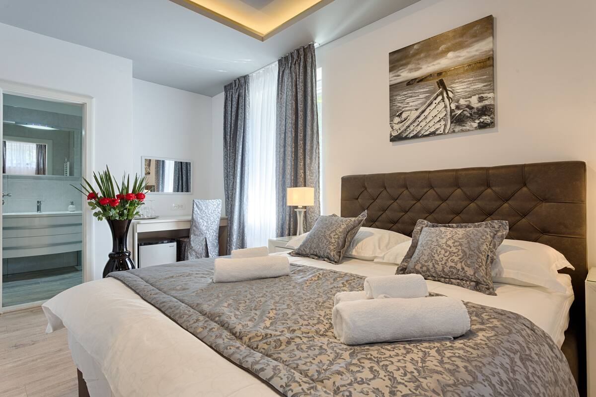 A hotel room with a large bed, a desk, a chair, a lamp, and a painting on the wall.