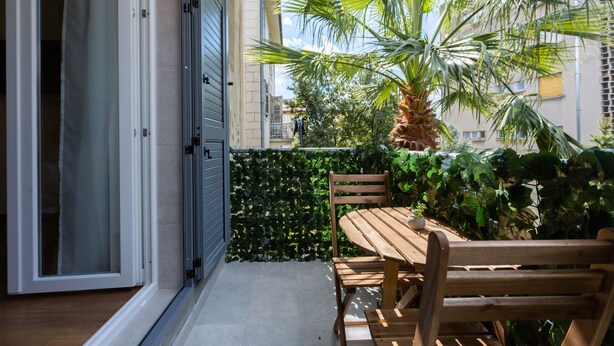 Un balcon avec une table et des chaises en bois, un palmier et une haie.