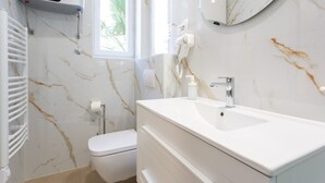Une salle de bain moderne avec un lavabo blanc, des toilettes, un porte-serviettes et un sèche-cheveux fixé au mur.