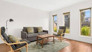 Ein modernes Wohnzimmer mit einem grauen Sofa, zwei gemusterten Sessel, einem Holztisch und einem grünen Teppich.