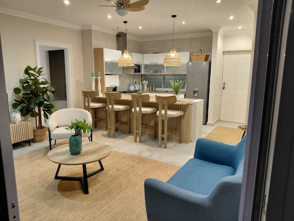 Un salon moderne avec un canapé bleu, une table basse ronde et un coin repas comprenant des chaises en bois et une petite table.