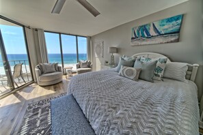 Ein geräumiges Schlafzimmer mit einem großen Bett, Meerblick und einem Balkon mit Sitzgelegenheit.
