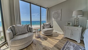 Ett modernt vardagsrum med en böjd soffa, ett runt sidobord och utsikt över stranden.