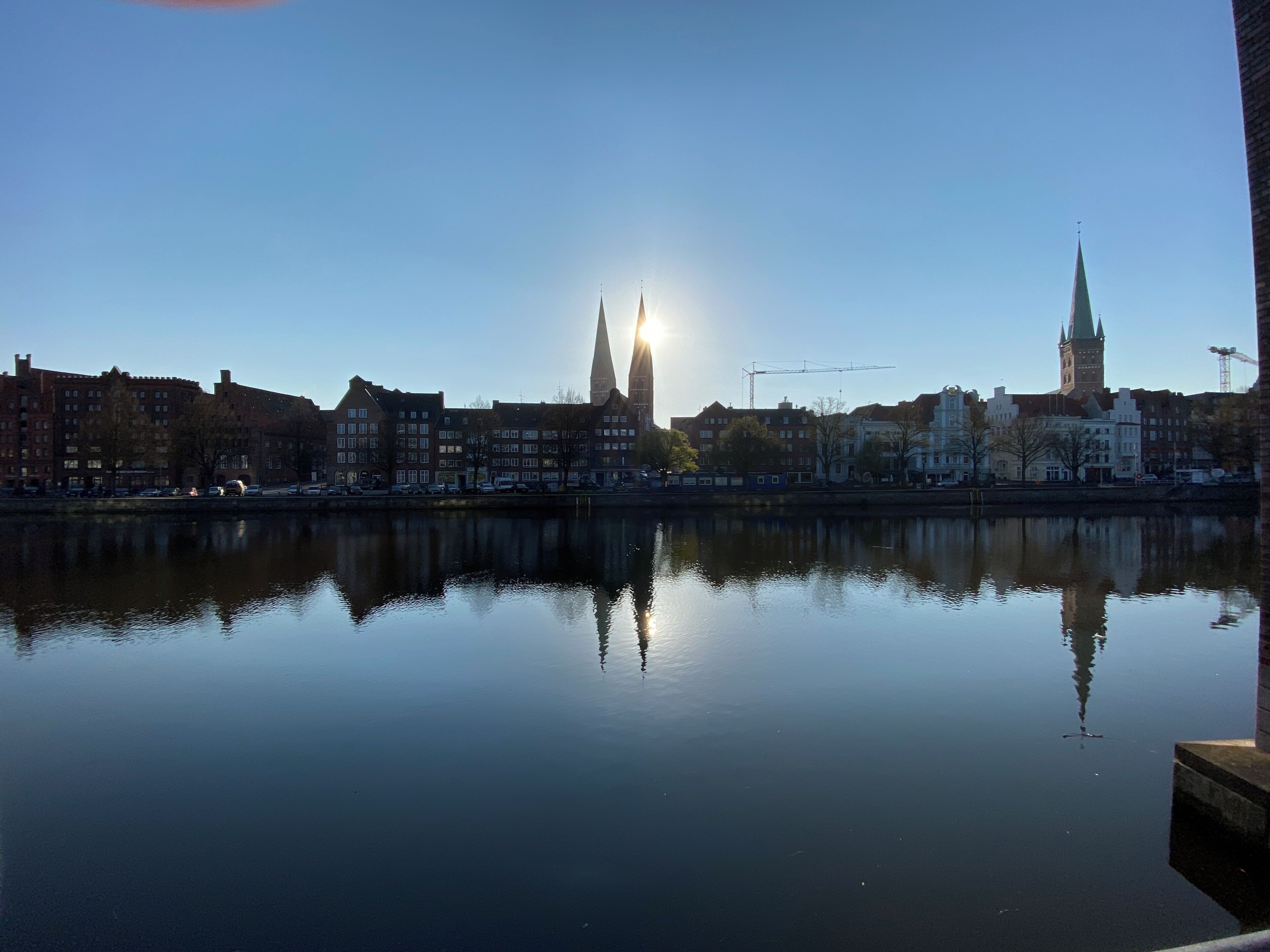 A calm river reflecting buildings and a tower under a clear sky.