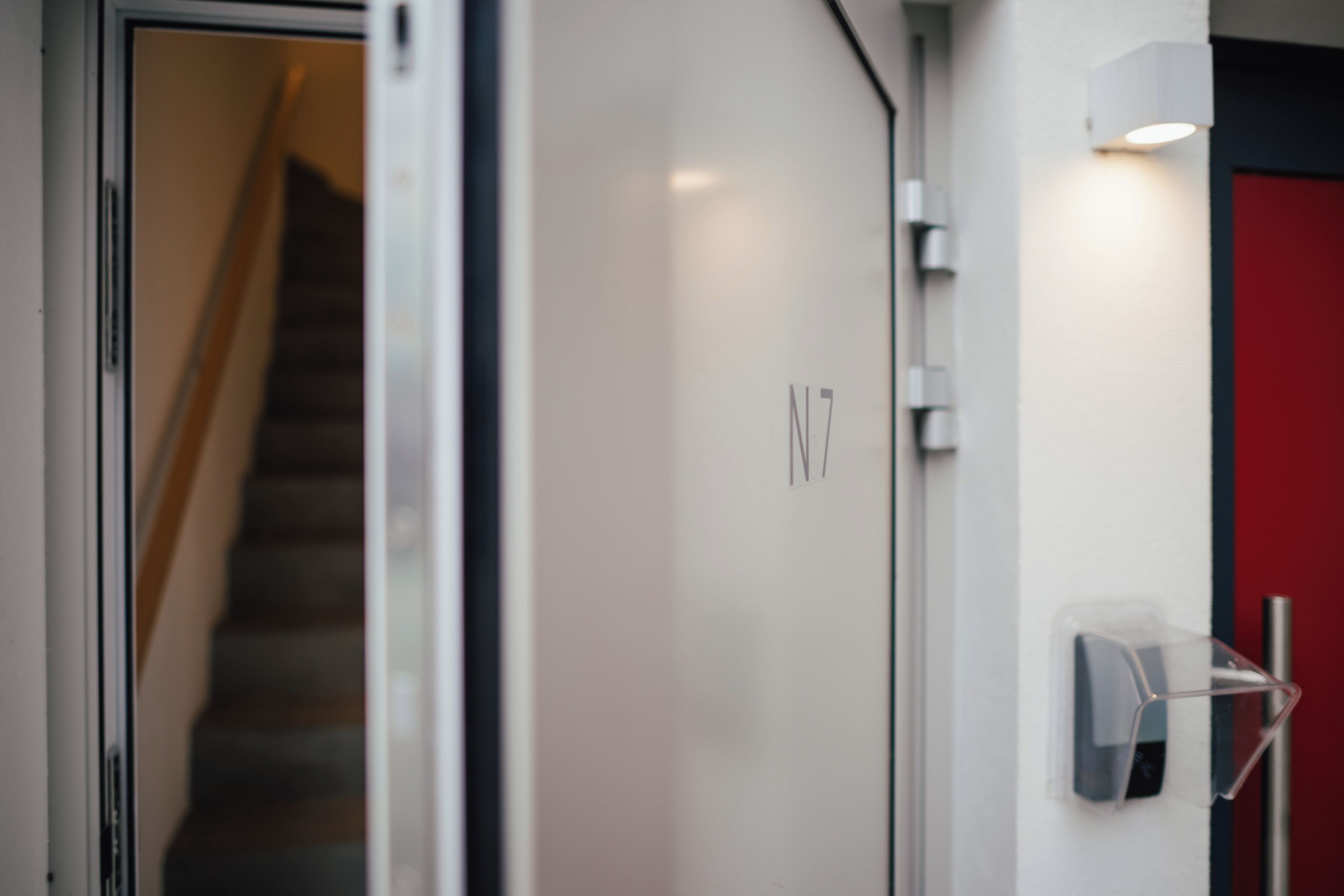 A modern interior with a staircase, a door labeled "N7", and a wall-mounted light fixture.