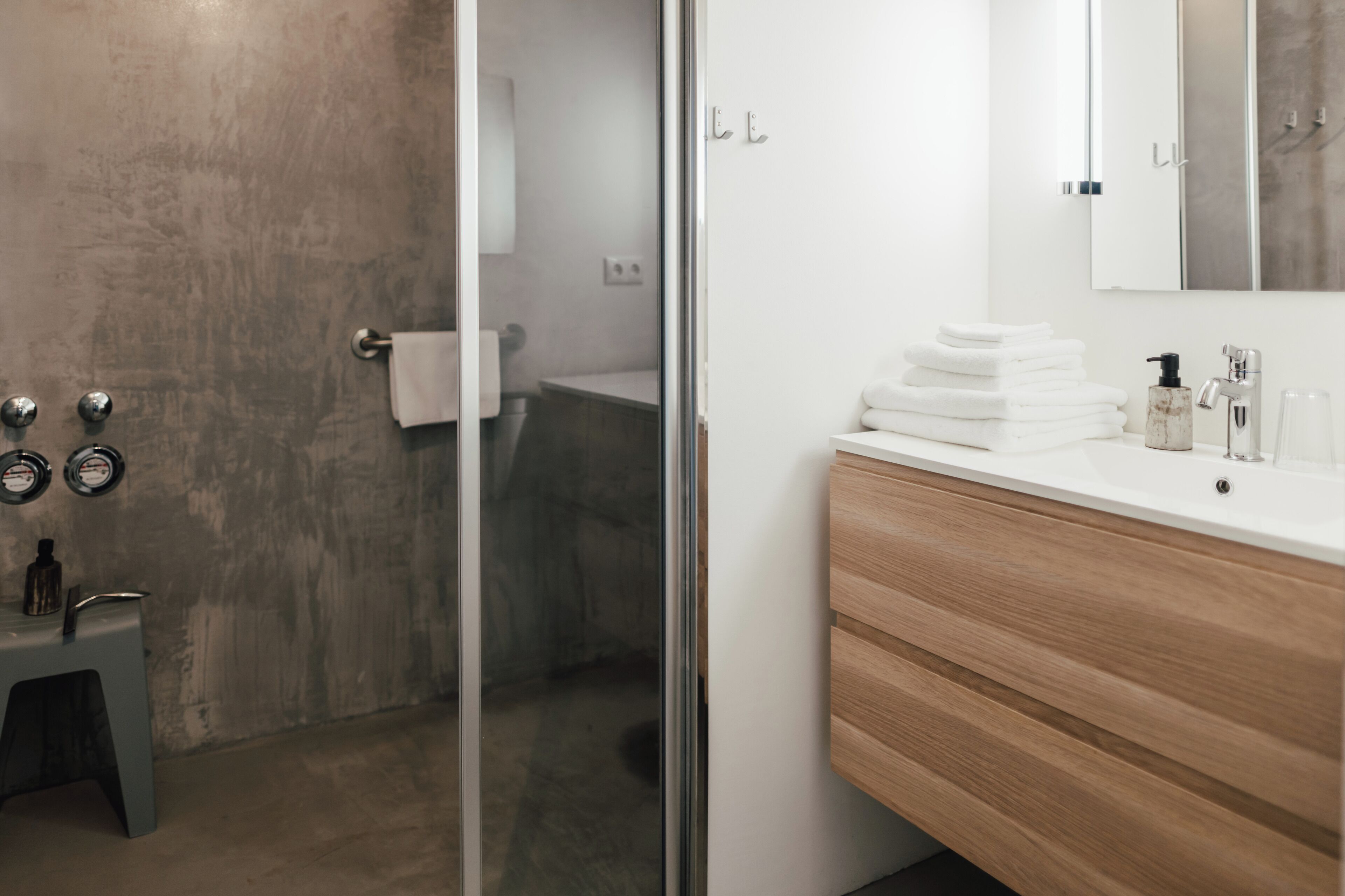 Un baño moderno con cabina de ducha de vidrio, tocador de madera con espejo y toallas ordenadas.