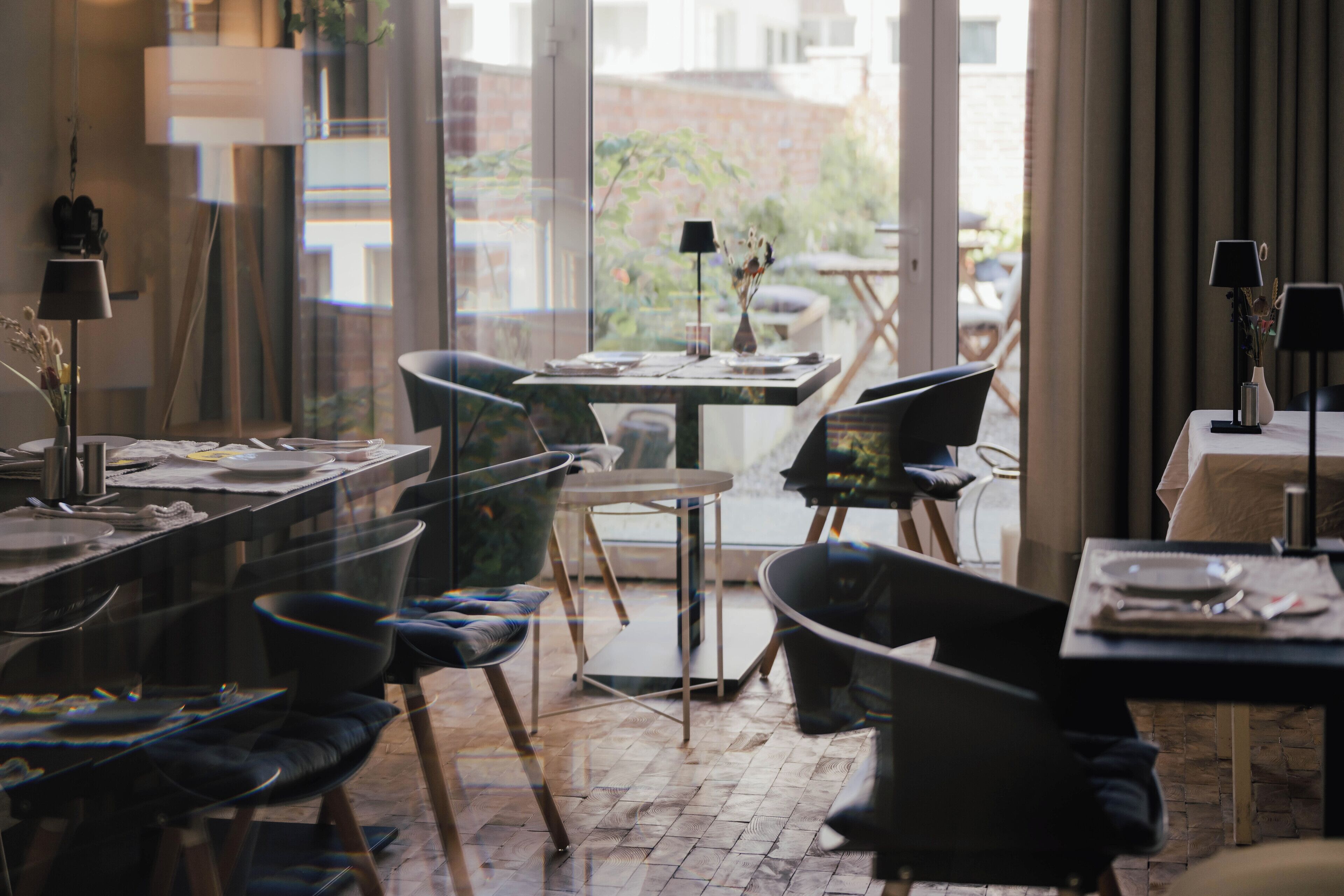 A dining area with modern furniture, a large window with a view of the outdoors, and a table set for a meal.