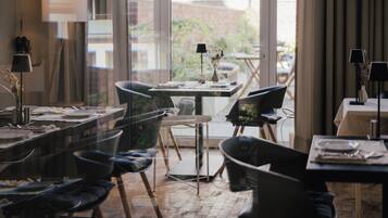 A dining area with modern furniture, a large window with a view of the outdoors, and a table set for a meal.