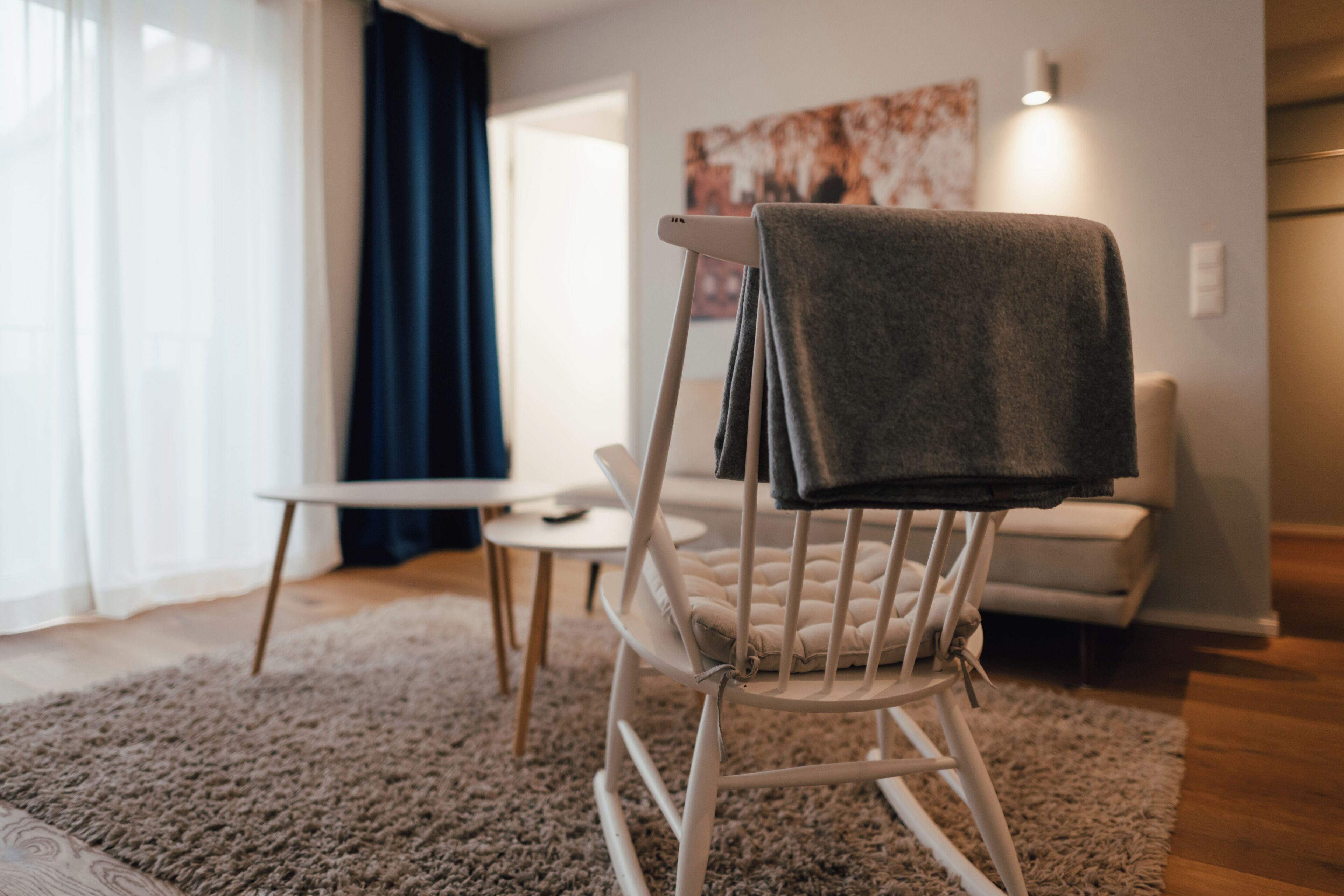 Een moderne woonkamer met een witte schommelstoel, een klein wit tafeltje en een beige bank.