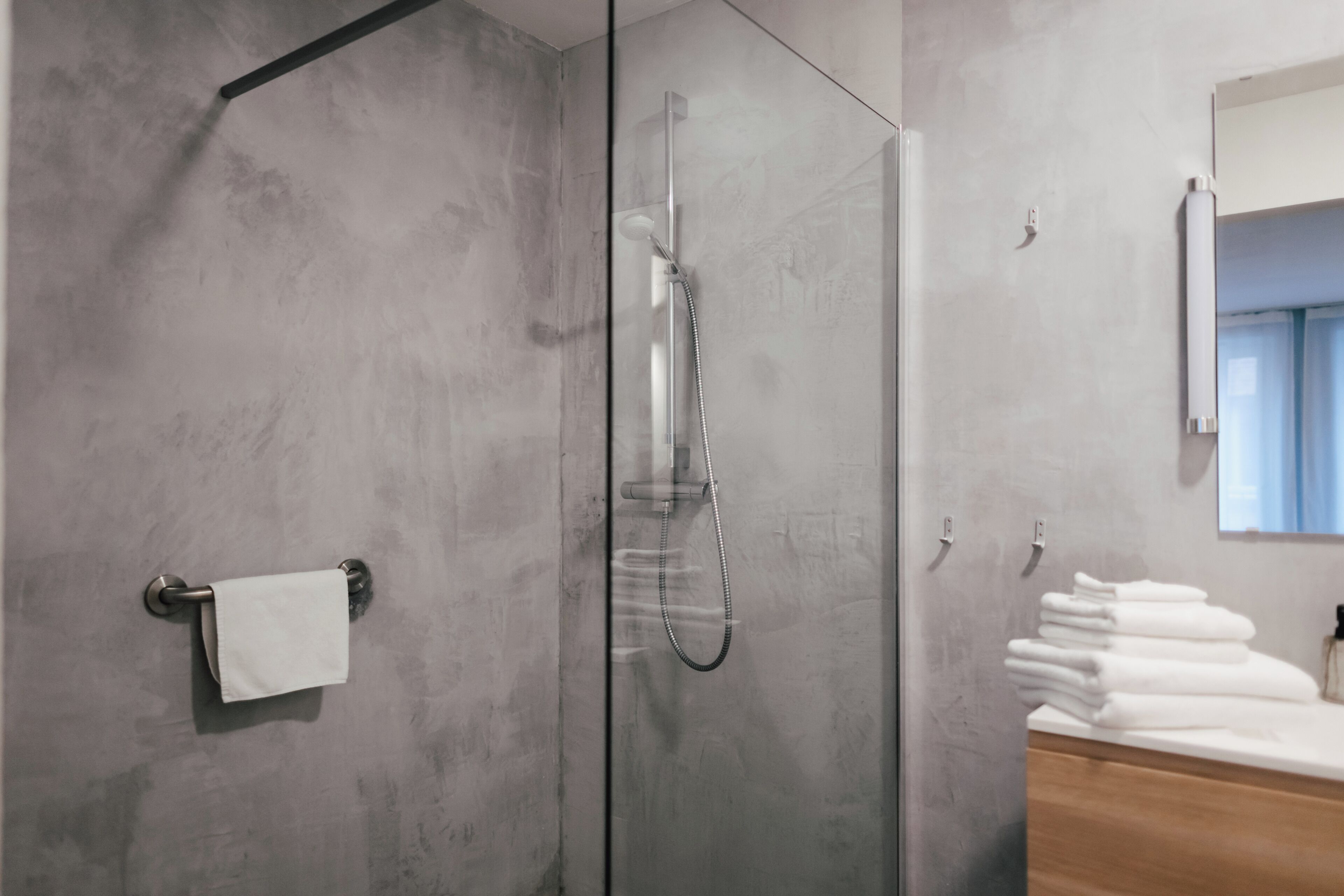 Ein modernes Badezimmer mit einer Glaskabine zur Dusche, einem Holzbadezimmer-Möbel und einem Stapel weißer Handtücher.
