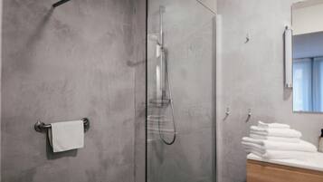 Ein modernes Badezimmer mit einer Glaskabine zur Dusche, einem Holzbadezimmer-Möbel und einem Stapel weißer Handtücher.