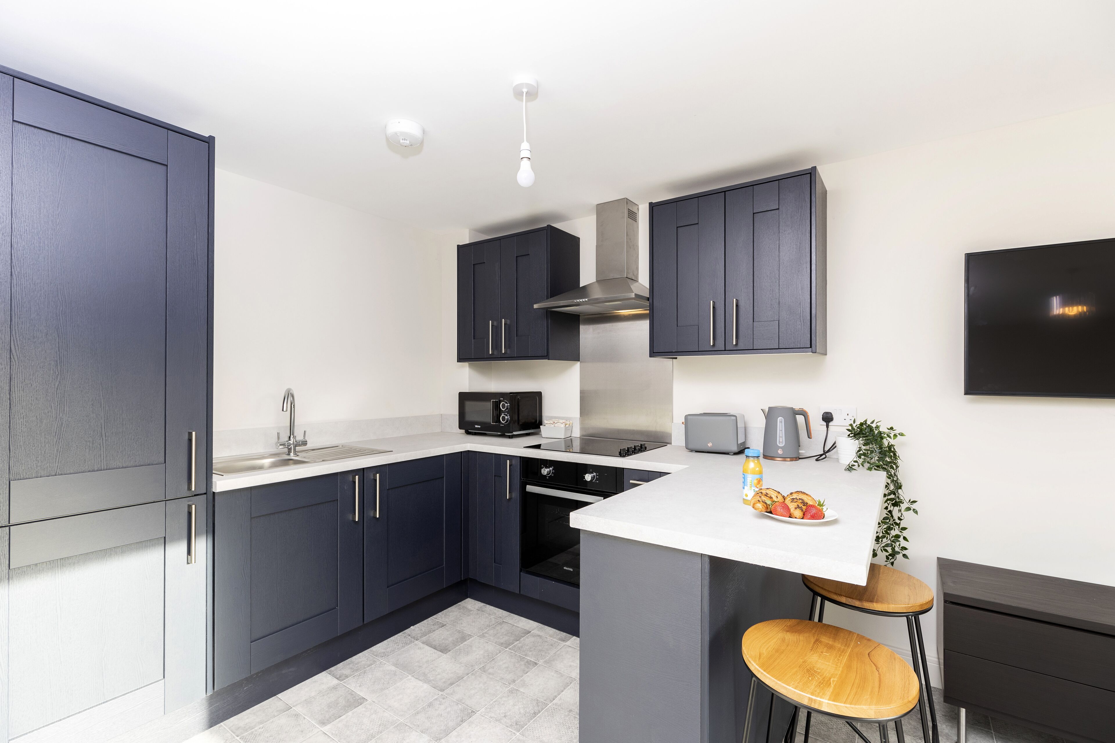 A modern kitchen with dark cabinets, a white countertop, a built-in oven, a microwave, and a small island with stools.