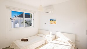 Ein Schlafzimmer mit zwei Betten, einem Fenster mit Blick auf Gebäude, einem Bild an der Wand und einem Deckenventilator.