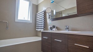 Ein modernes Badezimmer mit Badewanne, Waschtisch mit Spiegel und Handtuchhalter.