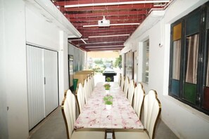 A corridor with a long table and chairs, a projector, and a window with curtains.