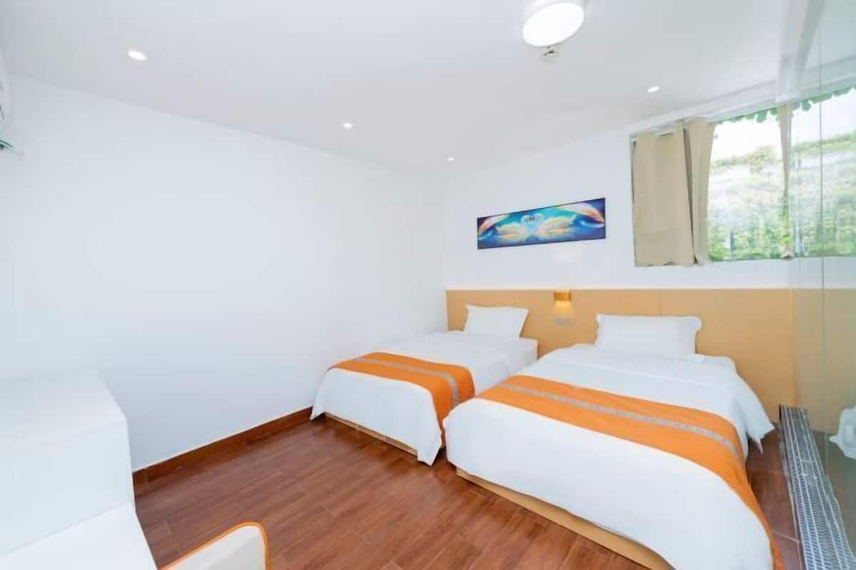 A hotel room with two beds, wooden flooring, a painting on the wall, and a window with curtains.