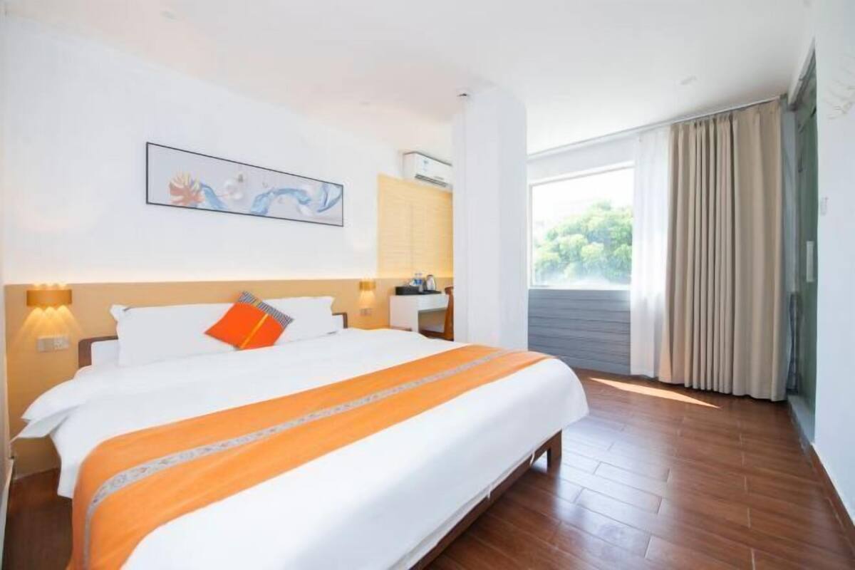 Habitación de hotel con una cama grande, un escritorio, una silla, una ventana con cortinas y un cuadro en la pared.