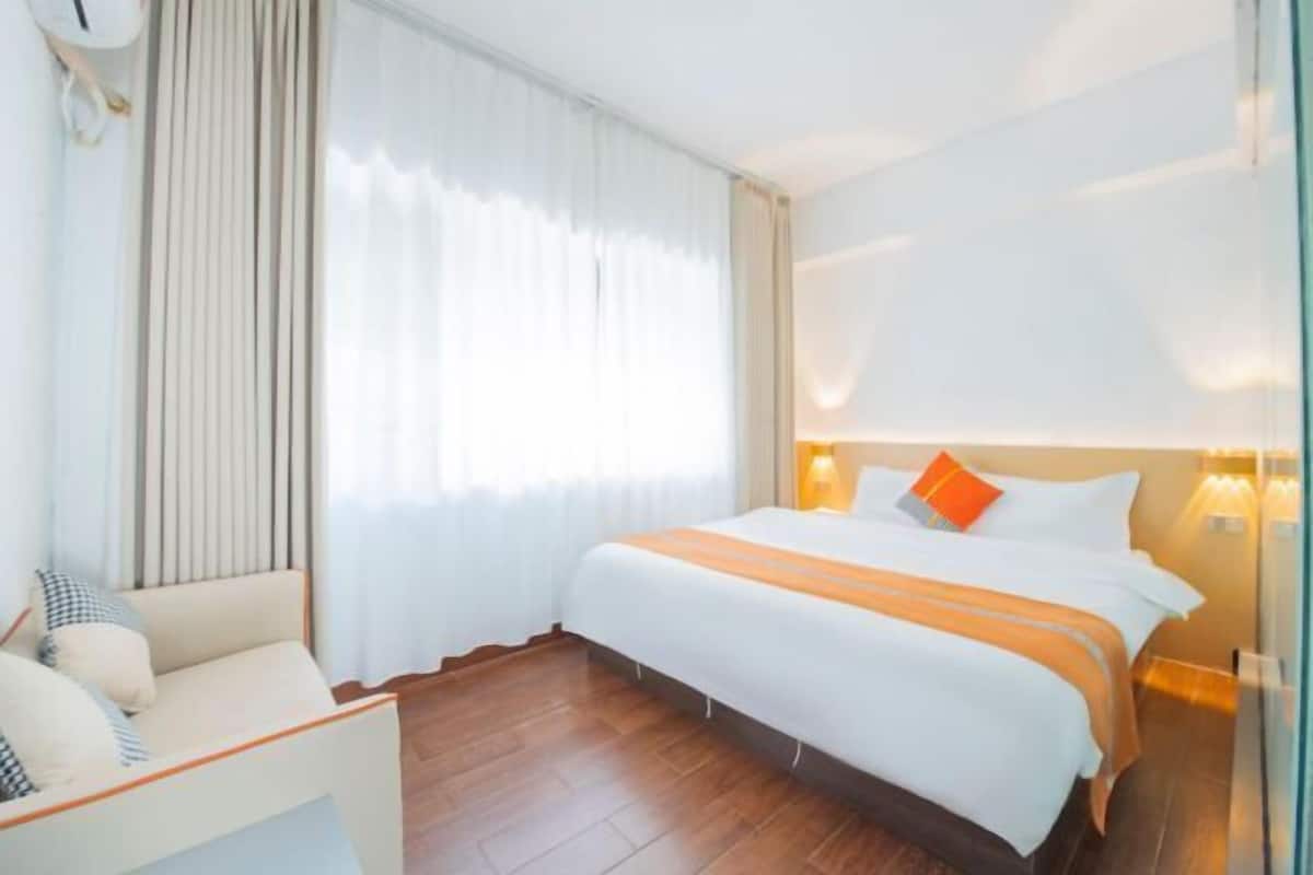 Habitación de hotel con cama, una silla, ventana con cortinas y mesita de noche con lámpara.