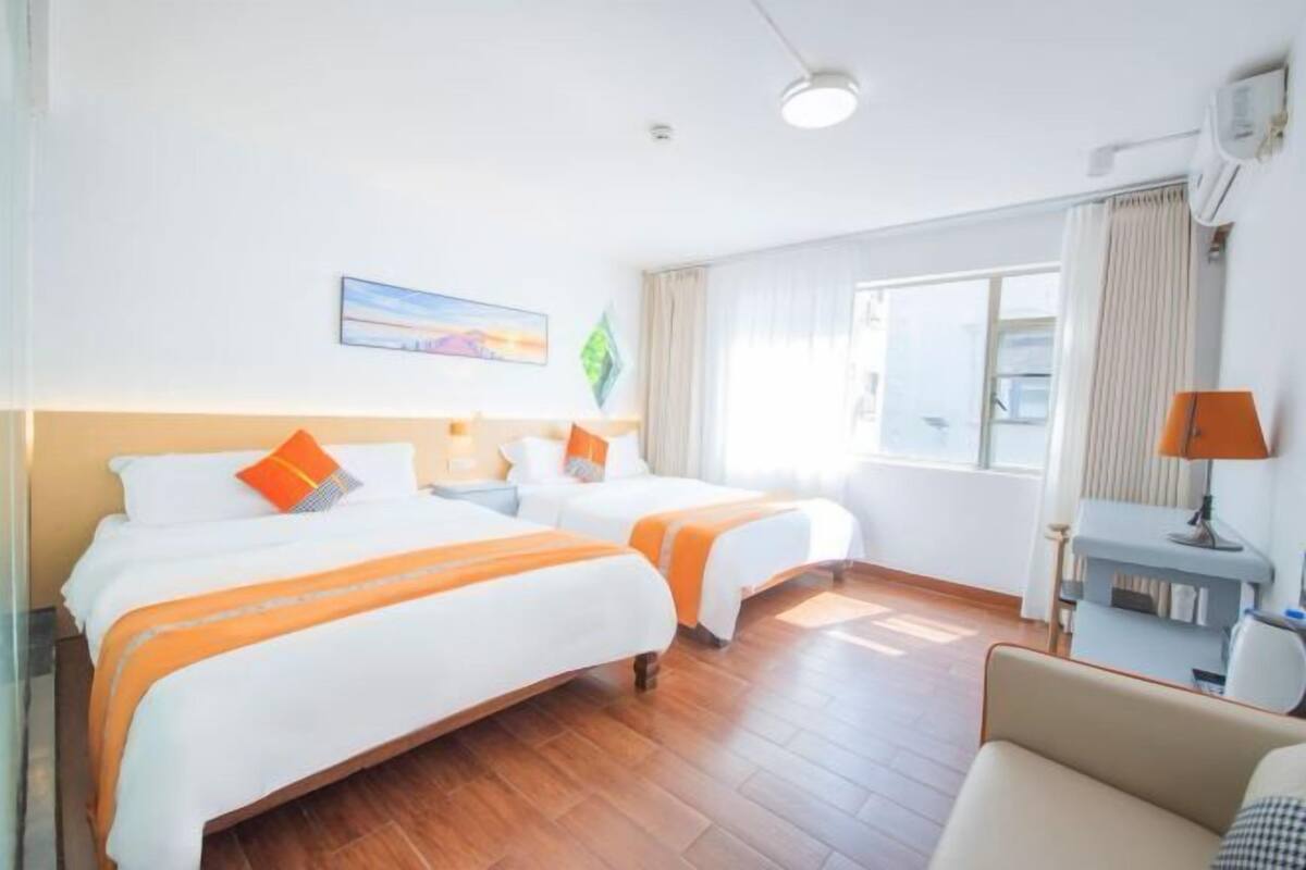 Habitación de hotel con dos camas, un escritorio, una silla y un ventanal amplio.
