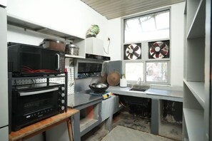 A compact kitchen with a microwave, oven, and sink. There is a window with blinds and a small plant on the counter.