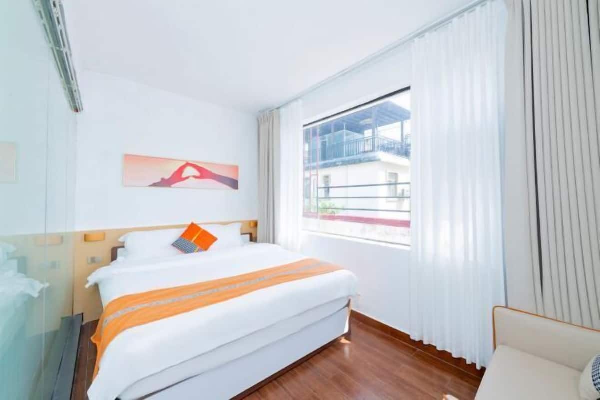 Una habitación de hotel con cama, una ventana con cortinas, un cuadro en la pared y vistas a edificios.