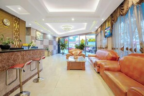 A hotel lobby with a reception desk, bar stools, a sofa, and a television. - Zihong Hotel (Yuxi)