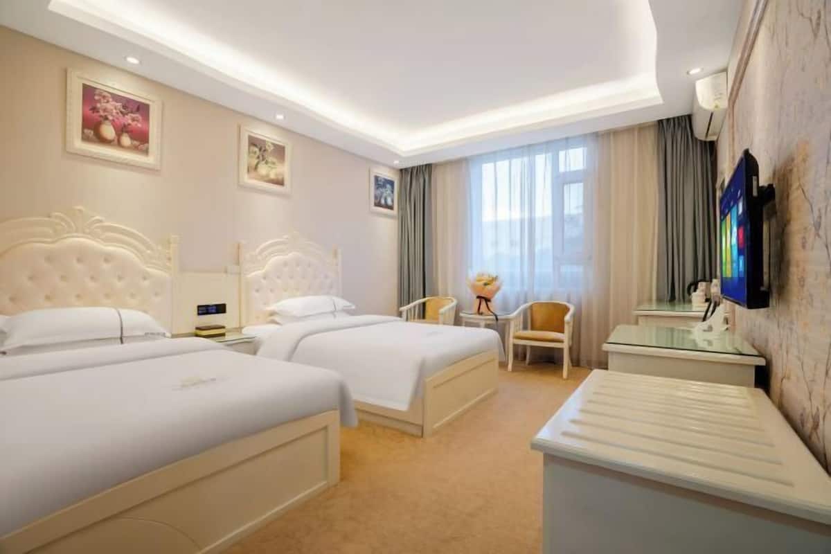 A hotel room with two beds, a TV, a desk, and a chair.