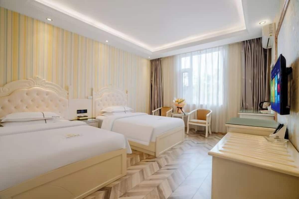 A hotel room with two beds, a small desk, a chair, and a television.