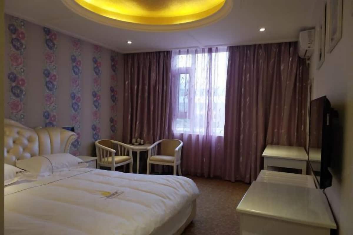 Une chambre d’hôtel avec un grand lit, une petite table avec des chaises, une télévision et une fenêtre avec des rideaux.