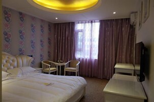 Habitación de hotel con una cama grande, una mesita con sillas, televisión y ventana con cortinas.