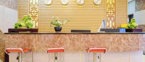 A reception area with a marble counter, three red bar stools, and decorative wall panels.