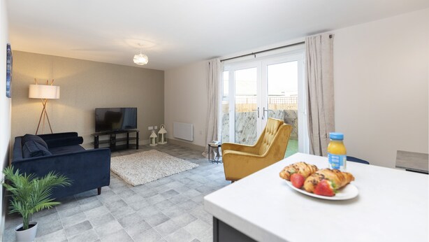 Ein modernes Wohnzimmer mit Sofa, Fernseher und Esstisch mit Speisen.