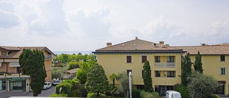 Un immeuble résidentiel avec un toit recouvert de tuiles, un balcon et un espace de stationnement où un fourgon est garé devant.