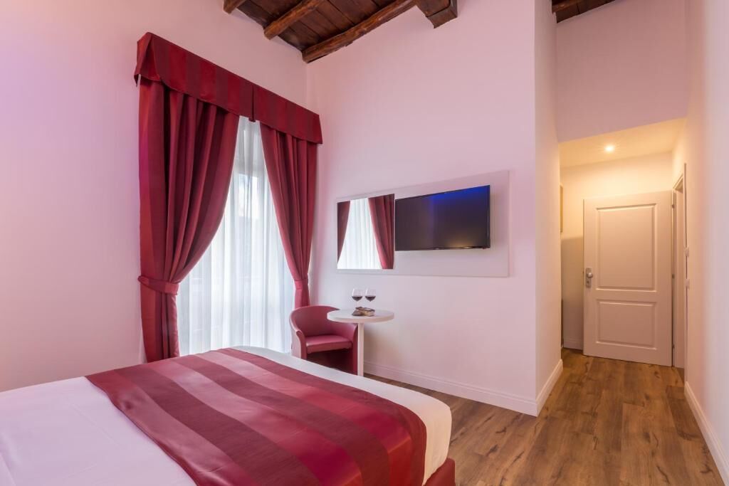 Een slaapkamer met een bed, een stoel, een klein tafeltje met glazen en een televisie aan de muur.