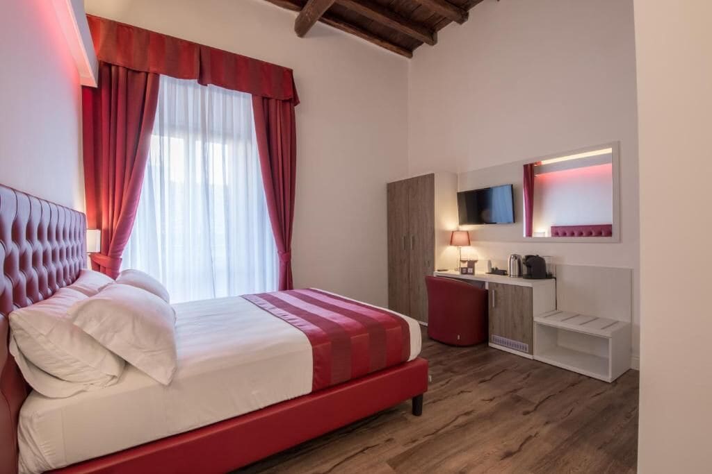 A hotel room with a bed, a desk, a mirror, and a television.