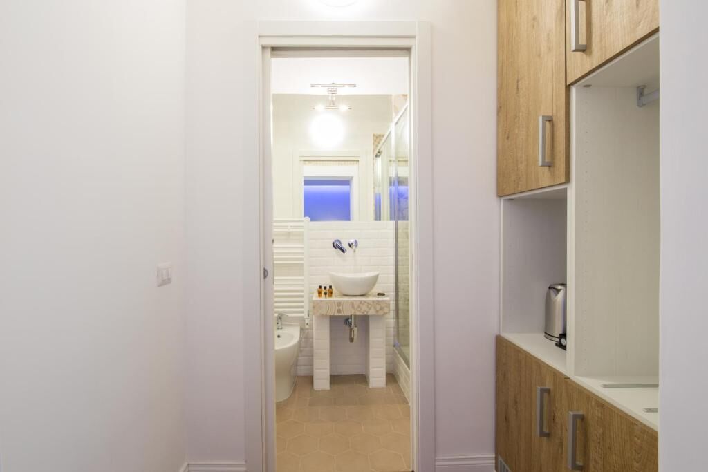 A narrow hallway leading to a bathroom with a white sink, mirror, and wooden cabinets.