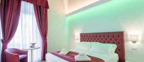A hotel room with a large bed, a small round table, a chair, and a nightstand.