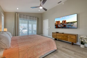A modern hotel room with a large bed, a ceiling fan, a flat-screen TV, a wooden cabinet, and a view of a marina. - VILLA VANITY – HEATED POOL & SPA | GULF ACCESS | BOAT RENTAL + TOURS VOUCHER INCL. (Cape Coral)