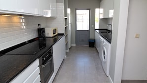 Una cocina con armarios blancos, encimera negra, microondas y lavadora.