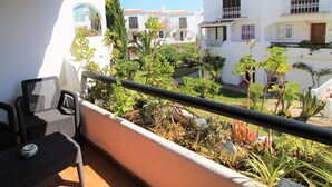 Un balcón con mobiliario de mimbre, vista a un patio con plantas y edificios.