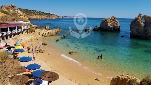 Una playa con agua cristalina, formaciones rocosas y sombrillas.